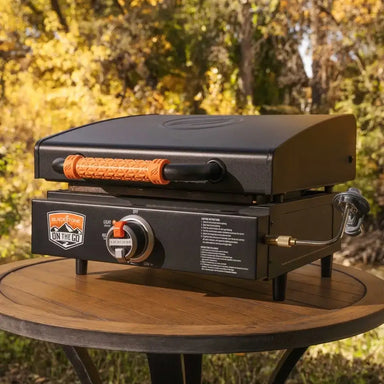 Outdoor portable griddle with closed hood on wooden table surrounded by fall trees