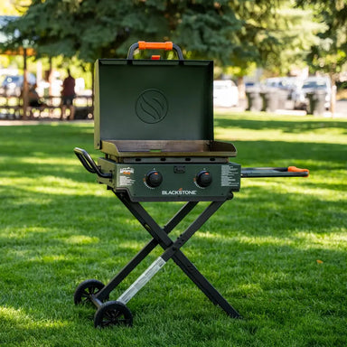 Blackstone 22-inch griddle with hood and folding legs set up outdoors on grass, perfect for portable grilling