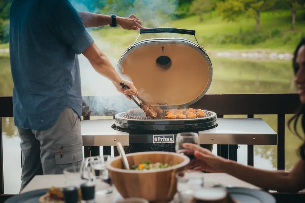 Man grilling steaks and wings on Primo ceramic grill by the lake