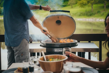 Man grilling steaks and wings on Primo ceramic grill by the lake