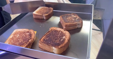Grilled cheese sandwiches cooking on Le Griddle stainless steel flat-top.