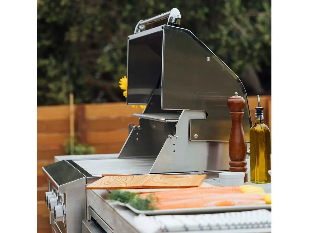Lifestyle shot of luxury outdoor grill with lid open next to sunflowers and food prep area.