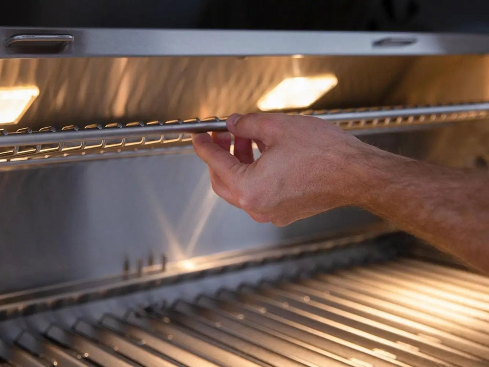 Hand adjusting warming rack inside illuminated gas grill
