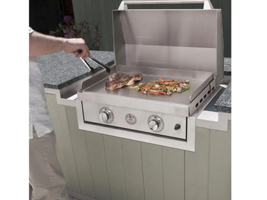 Person grilling steak and vegetables on a stainless steel Le Griddle built-in gas griddle with lid open.