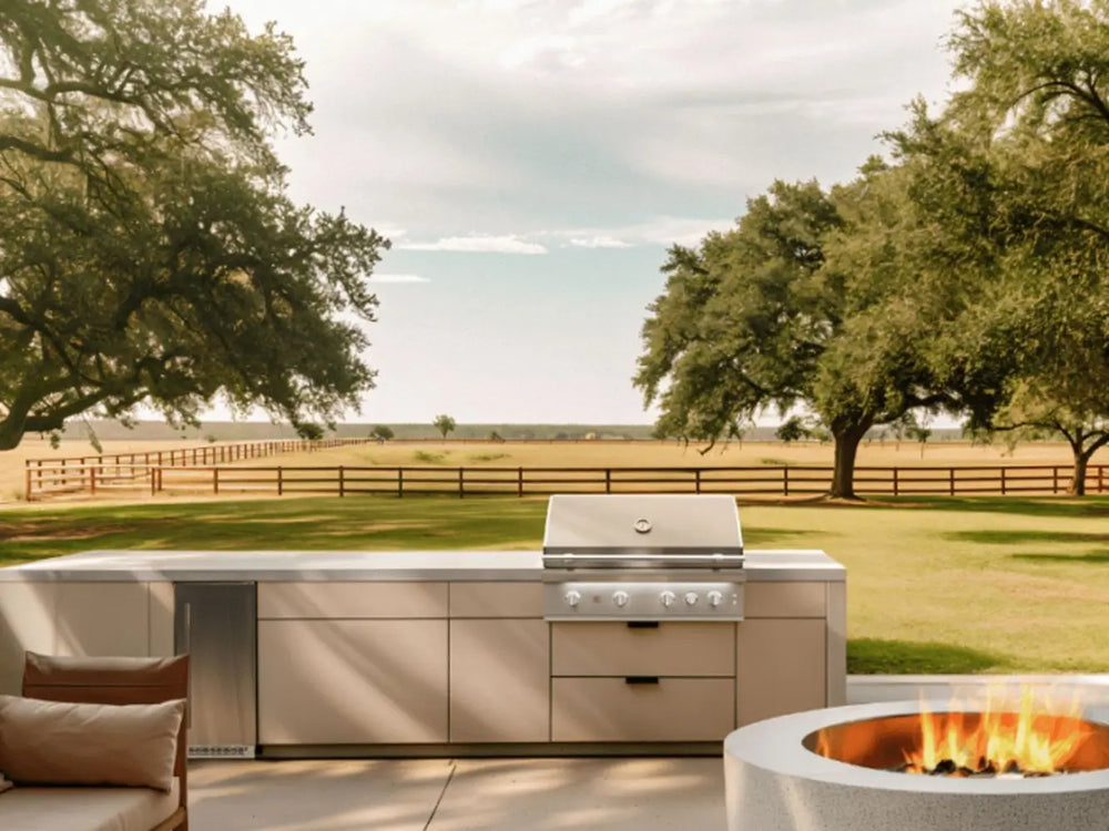 Outdoor kitchen with stainless steel built-in gas grill and fire pit overlooking open field.