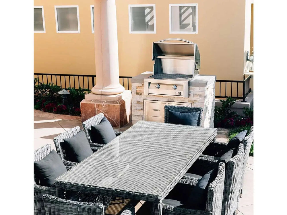 Patio dining area with wicker table and chairs next to stainless steel built-in gas grill.