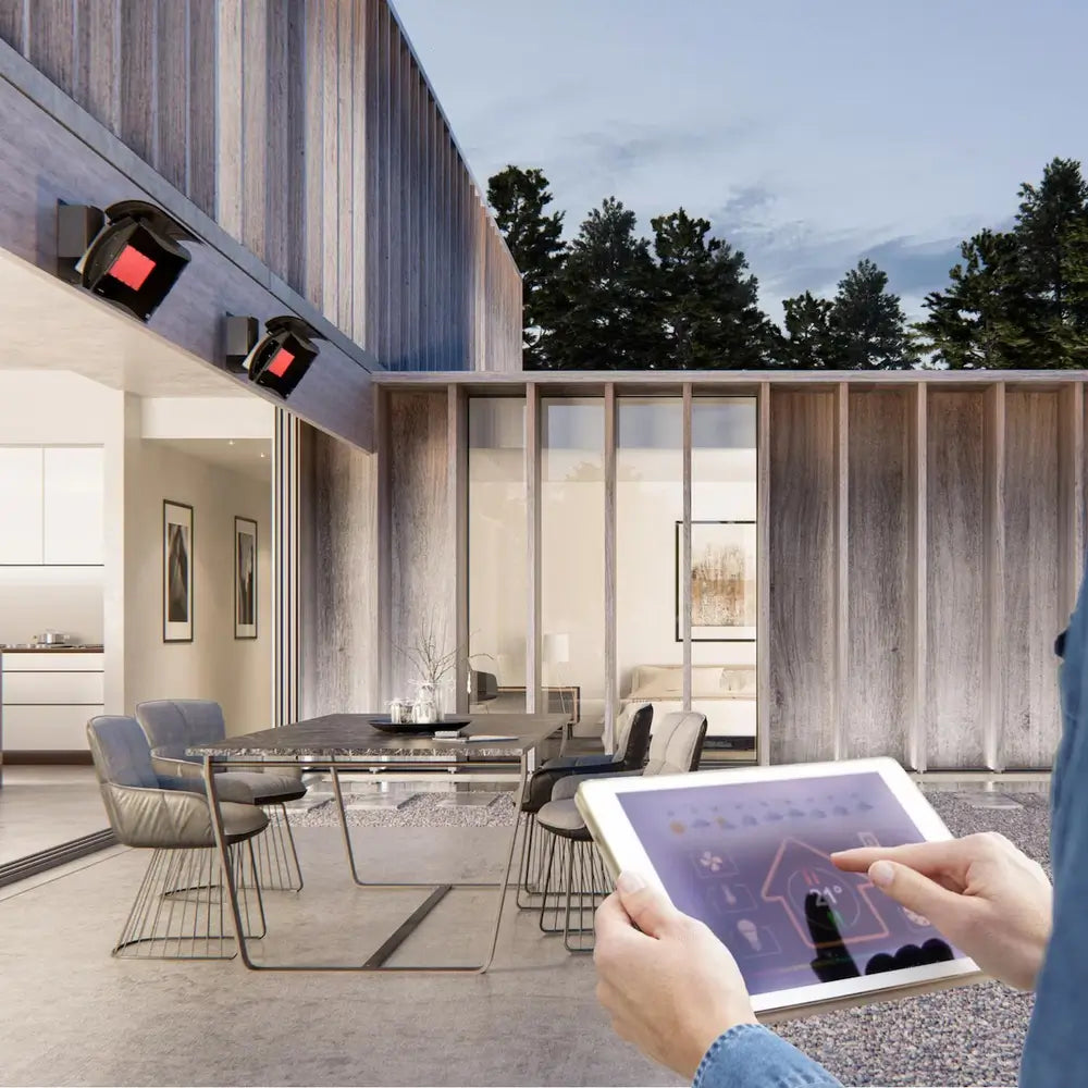Person controlling Bromic electric patio heaters via a tablet app, demonstrating smart home automation with RS232 link.