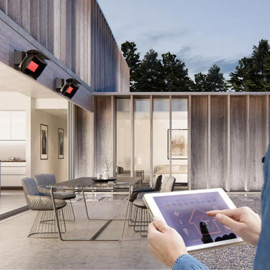 Person controlling Bromic electric patio heaters via a tablet app, demonstrating smart home automation with RS232 link.