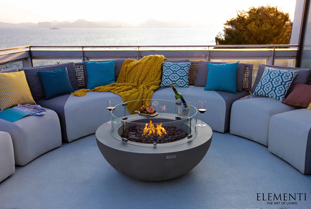 Luxury outdoor patio featuring a modern gray fire pit with glass wind guard and curved outdoor sofa seating.