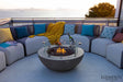 Luxury outdoor patio featuring a modern gray fire pit with glass wind guard and curved outdoor sofa seating.