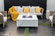 High-output 60,000 BTU Elementi Plus Bianco fire table on a white background, featuring a lit linear burner and decorative blue glass fire media.