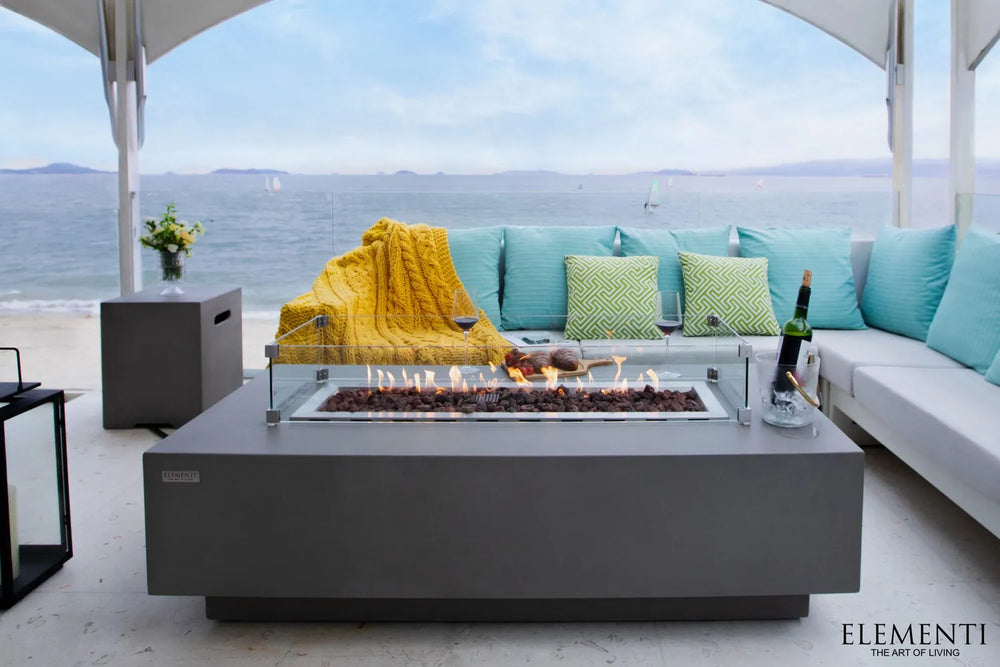 Beachfront patio featuring Elementi Granville OFG121LG Fire Table with glass wind guard and cozy decor.