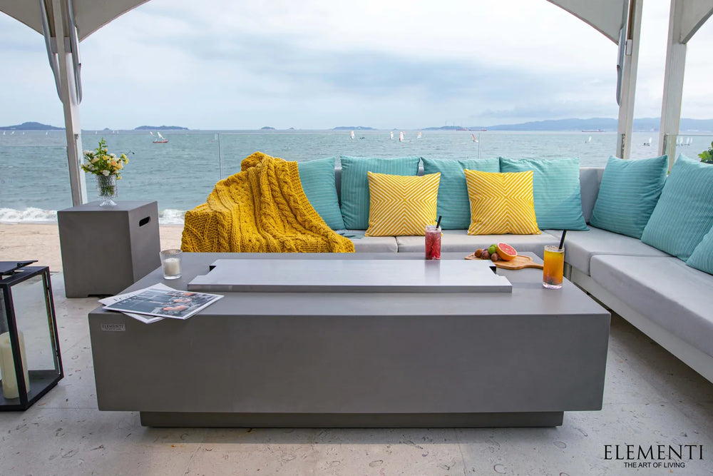 Elementi Granville OFG121LG Fire Table with stainless steel cover lid in a beachfront patio setting.