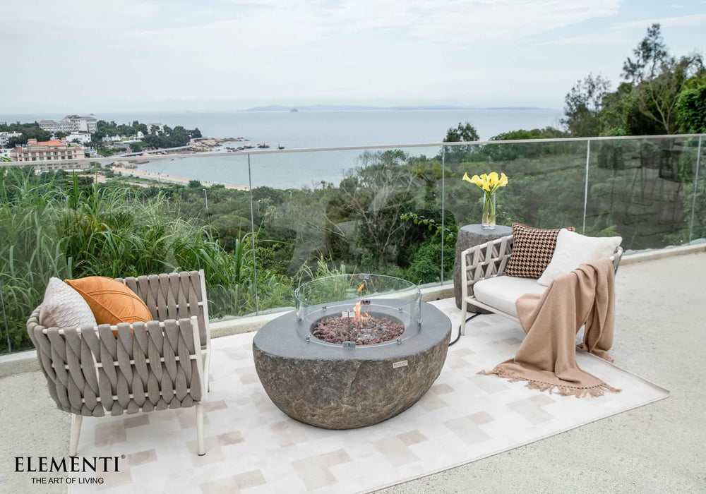 Elementi Boulder fire table equipped with a circular tempered glass wind guard for flame protection on a windy balcony.