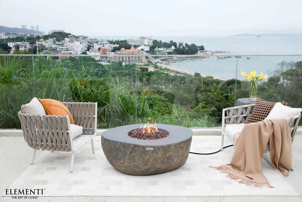 High-end outdoor patio set on a coastal balcony featuring the Boulder fire table as a naturalistic centerpiece.