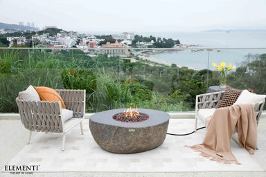 High-end outdoor patio set on a coastal balcony featuring the Boulder fire table as a naturalistic centerpiece.