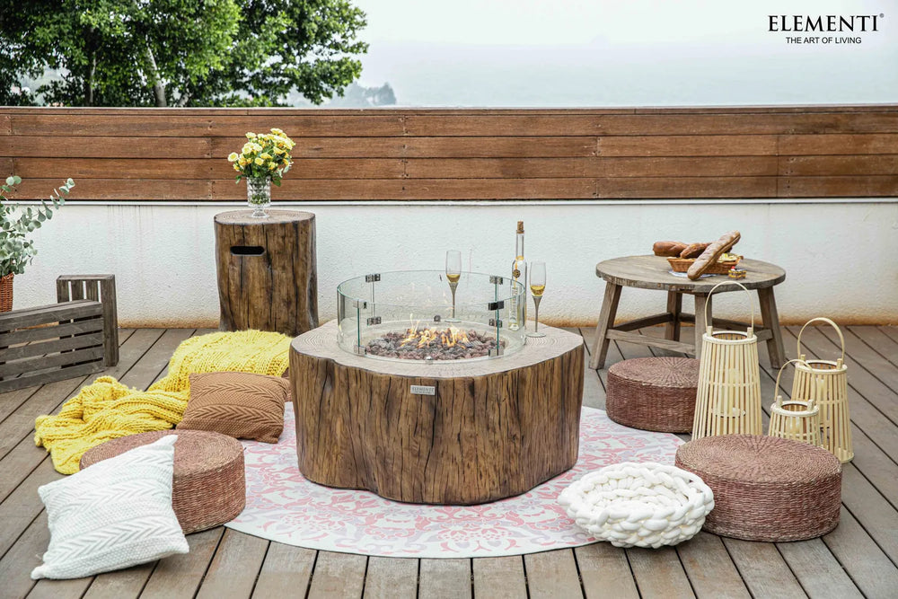 Rustic patio featuring an Elementi Manchester OFG145RW Fire Table 42" Red Wood with outdoor chairs and greenery.