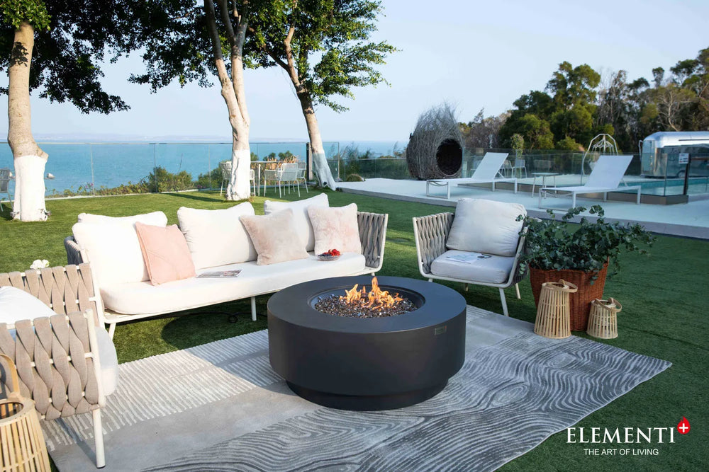 Elementi Plus Nimes dark gray fire table in outdoor lounge with sofa seating and ocean view.