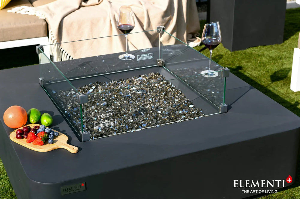 Glass wind guard on Elementi Plus Bergamo fire table with fire glass media and outdoor tabletop space.