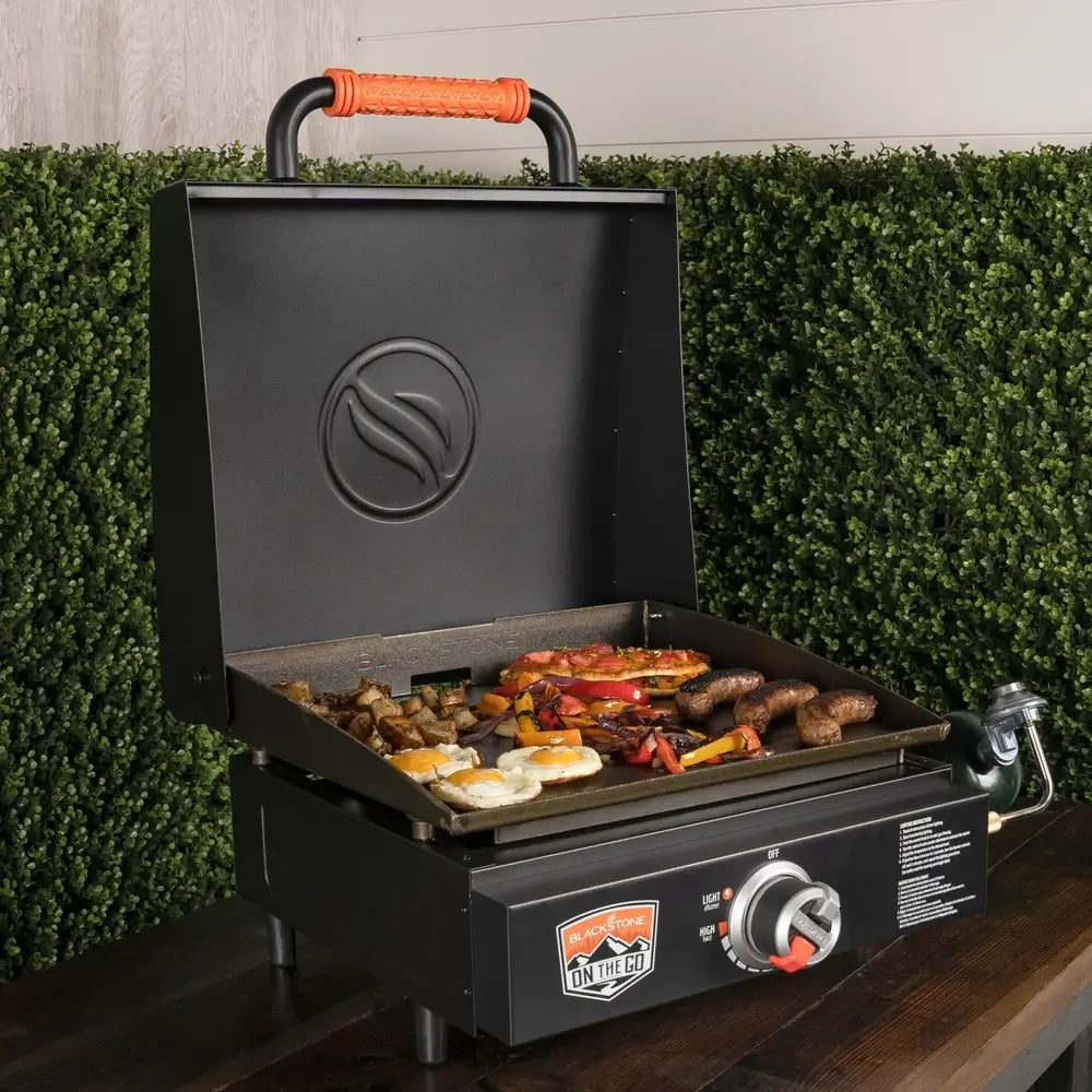 Open hood griddle cooking eggs, sausages, and veggies on outdoor patio table