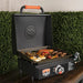 Open hood griddle cooking eggs, sausages, and veggies on outdoor patio table