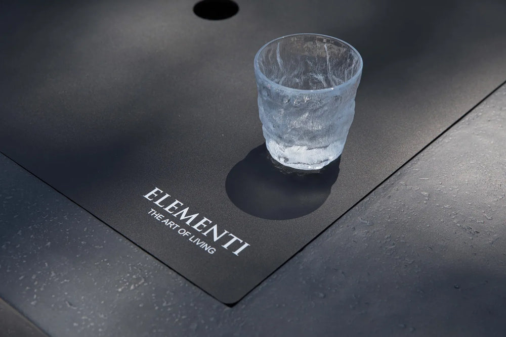 Elementi logo on dark gray fire table surface with burner cover installed.