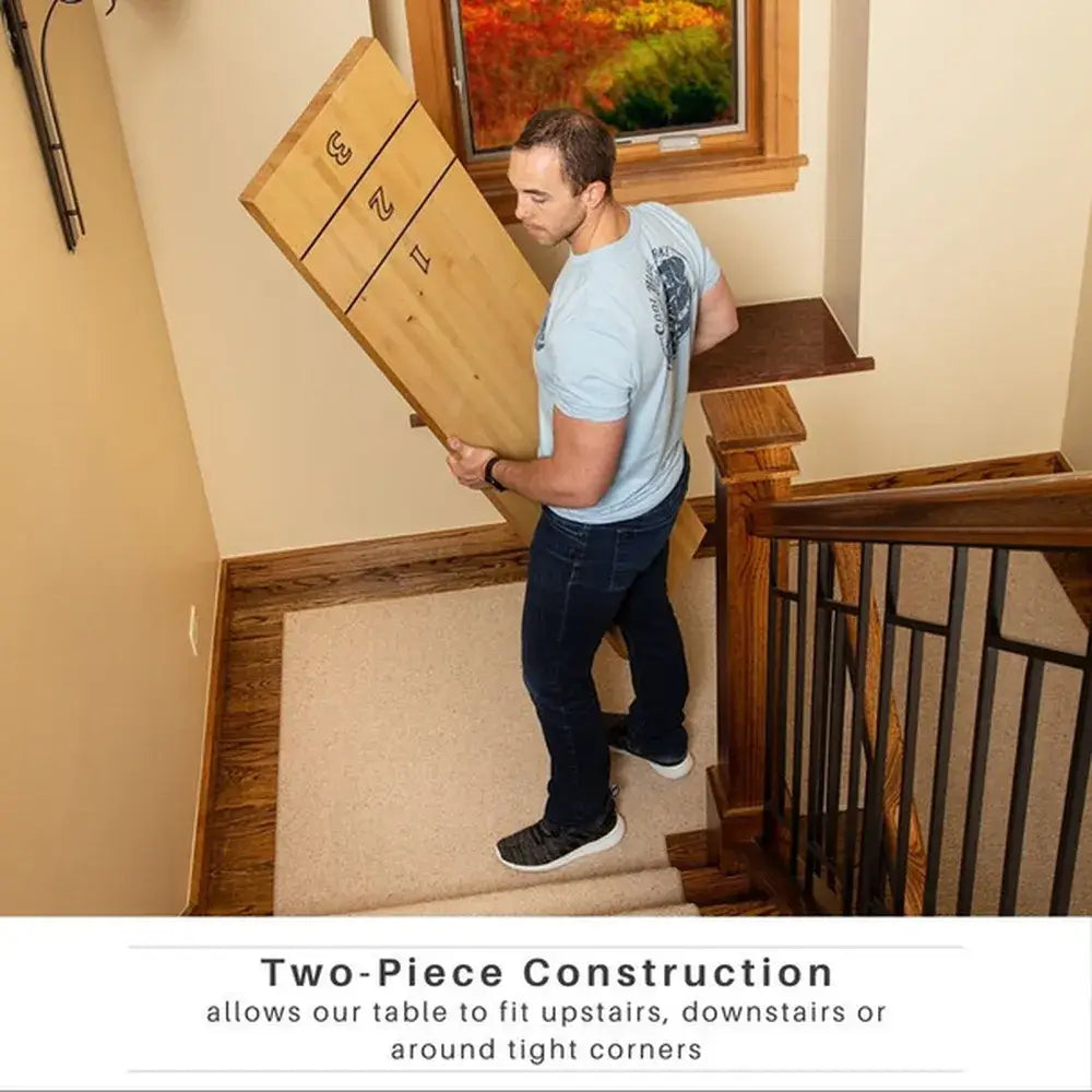 Man carrying one section of the Freetime Fun 2-Piece Shuffleboard table down stairs, demonstrating its easy maneuverability for tight corners.