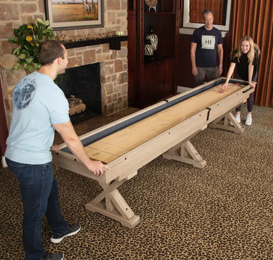 Three people enjoying the Freetime Fun Rustic Oak Shuffleboard Table in a stylish home environment.