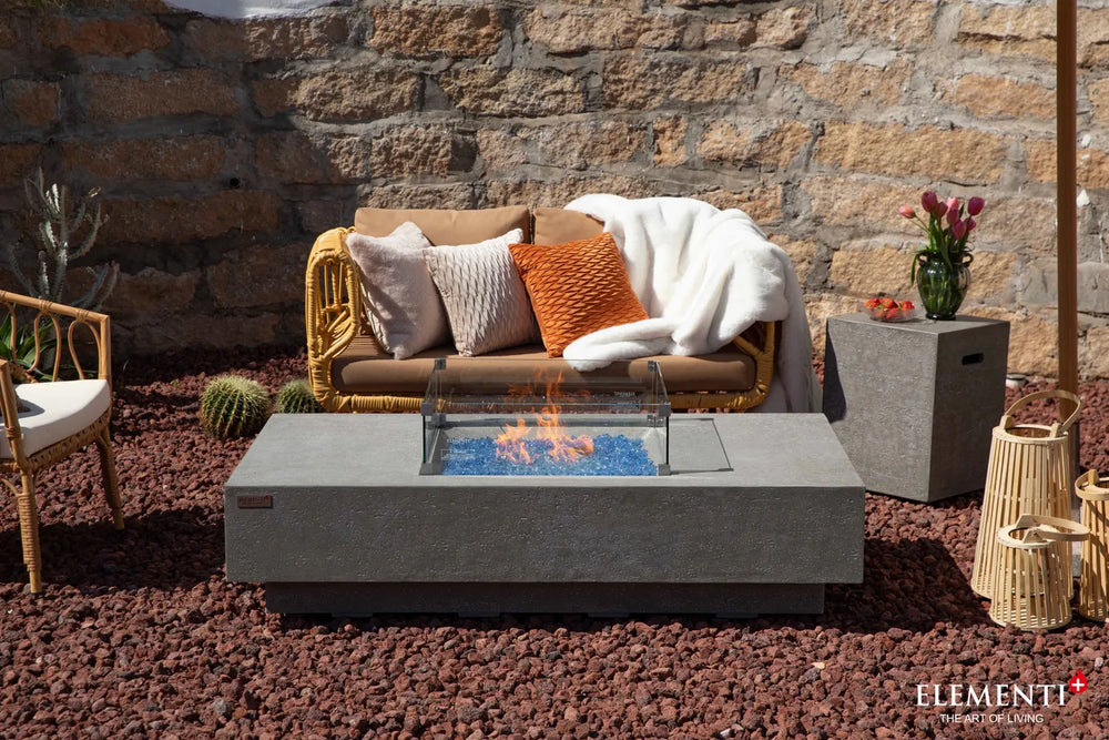 Elementi Plus Monte Carlo light gray fire table with glass wind guard in outdoor lounge setting.