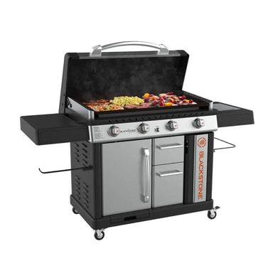 Blackstone 36-inch stainless steel propane griddle with hood, four burners, storage cabinet, and side shelves cooking burgers, veggies, and kabobs