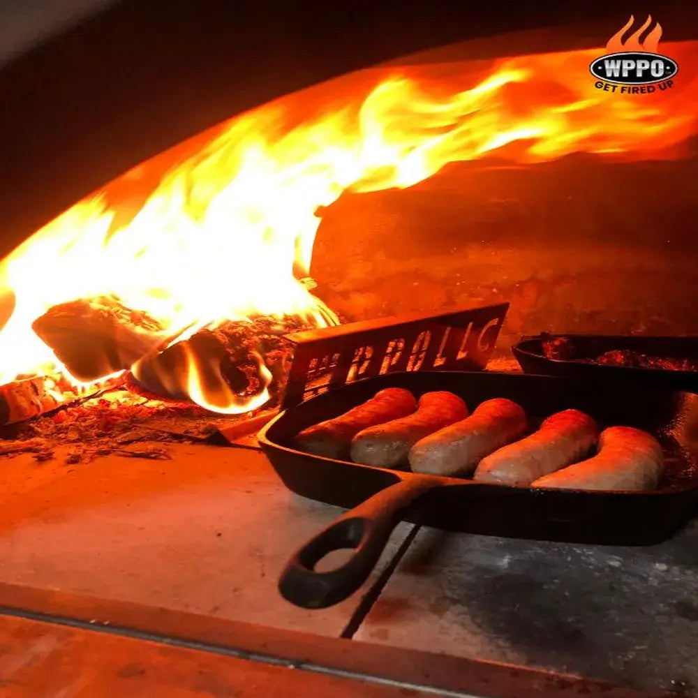 Cast iron skillet cooking sausages in WPPO Karma 55 commercial wood-fired oven with open flame and WPPO logo.