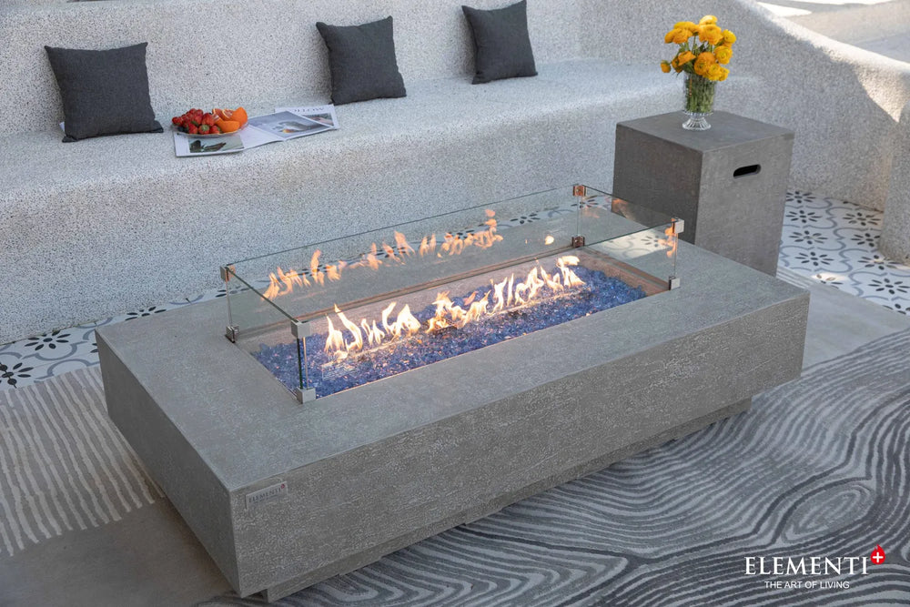 Elementi Plus Riviera fire table with glass wind guard and blue fire glass on patio.