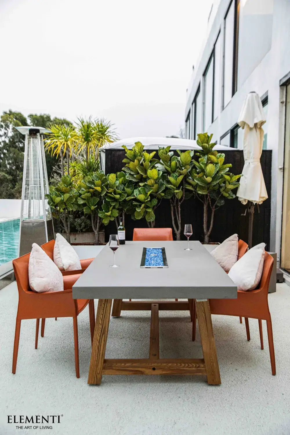Modern patio setting with the lit gray Elementi OFG201 Sonoma Dining Fire Table and scenic backyard view.