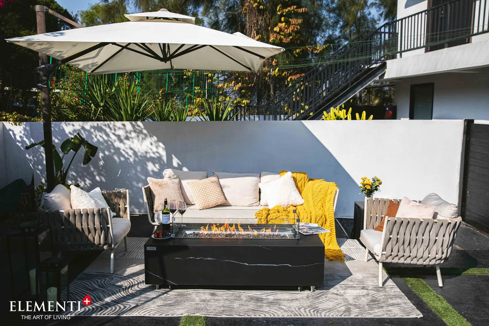 Elementi Plus OFP121BB Varna Bulgaria Black 60,000 BTU square fire table with a dark charcoal porcelain finish, styled on a luxury poolside patio with modern white lounge chairs.