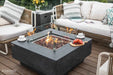 Elementi Manhattan fire table equipped with a clear tempered glass wind guard for flame protection on a windy patio.