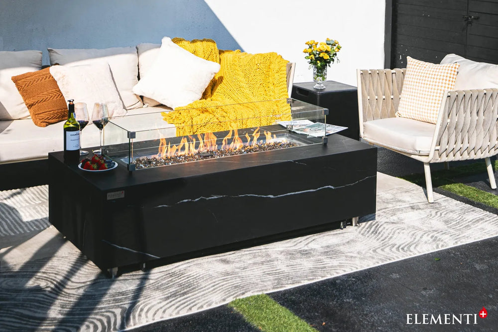 Detail shot of the Varna Bulgaria Black fire table used as a luxury coffee table with the burner lid in place, styled with a wine bucket, champagne, and snacks.