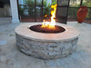 Side profile of the Travertine TessaRai 46" Round Gas Fire Pit showing the textured stone base and high-quality burner flames in an outdoor living space.