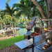 Tagwood BBQ06SS Argentine grill outdoor setup beside canal with palm trees and boat dock