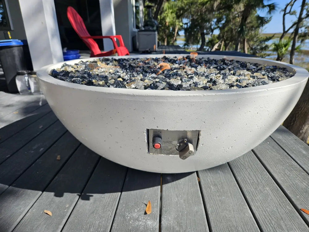 Travertine TessaRai 40 inch Patio Fire Pit Kit with fire glass and manual control panel on outdoor deck overlooking marsh view