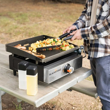 Man cooking vegetables and sausages on the Blackstone 17-inch stainless steel griddle, showcasing its spacious flat top cooking surface for versatile outdoor meals.