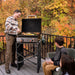 Family grilling on Blackstone 22" portable propane griddle with hood on wooden deck in autumn backdrop