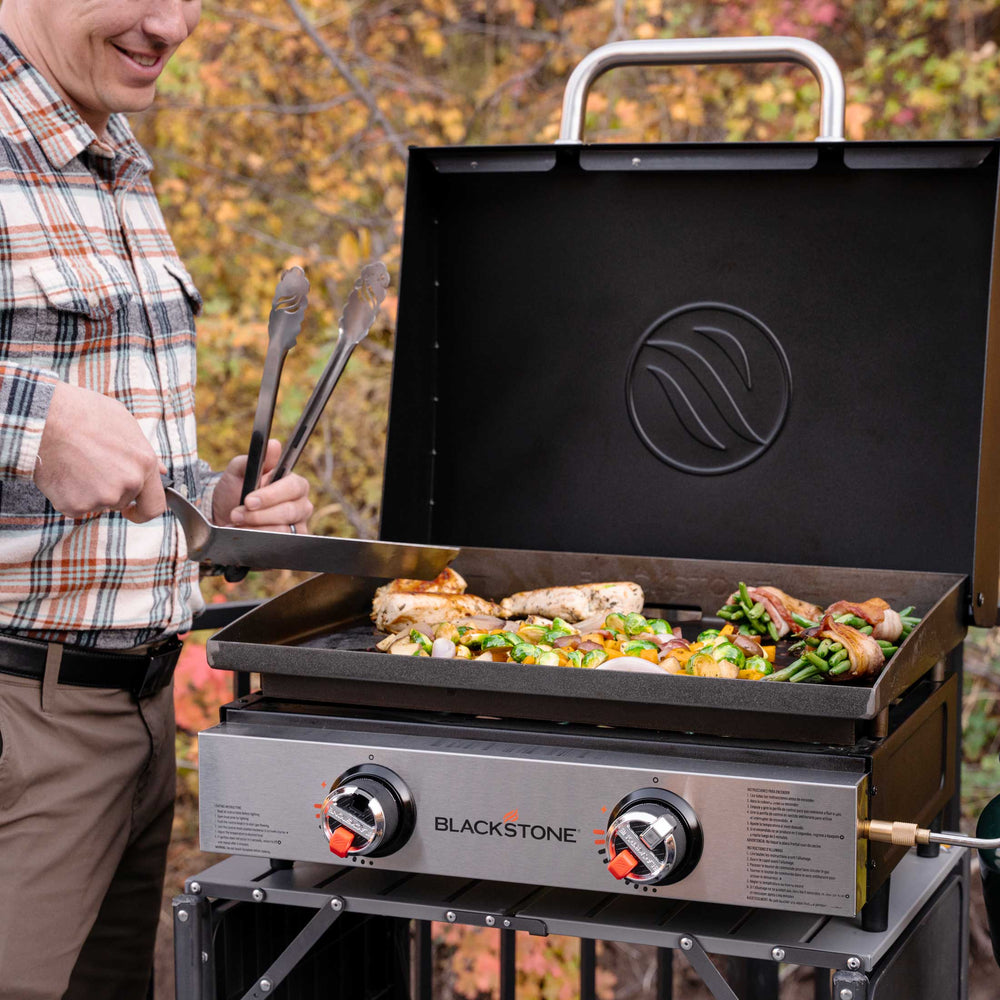 Man grilling chicken and vegetables on Blackstone 22" tabletop griddle with hood in outdoor setting