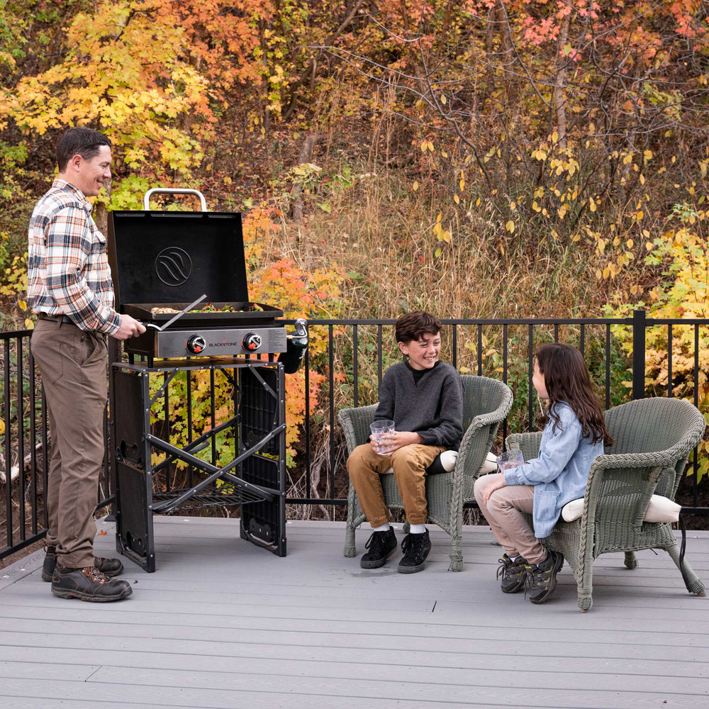 Outdoor patio cooking with Blackstone 22" portable griddle and hood while kids relax on wicker chairs