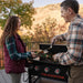 Man serving grilled food from Blackstone stainless steel griddle with hood to woman on patio – high-performance griddle for home chefs