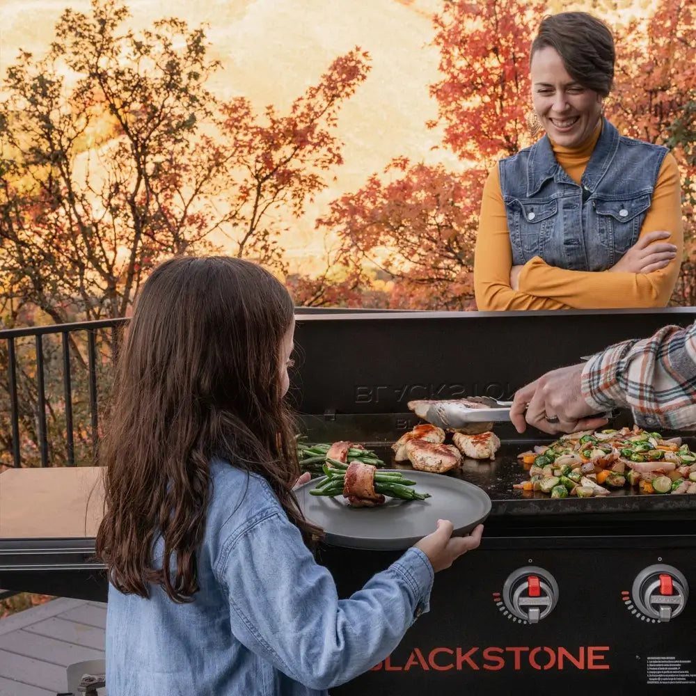 Child waiting for grilled food at Blackstone outdoor griddle station with mom smiling in background – family-friendly backyard grilling