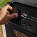 Hand adjusting temperature dial on Blackstone 900 Pellet Grill digital control panel with wood pellets in visible hopper