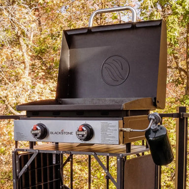 Blackstone 22" tabletop propane griddle with hood and dual burners on collapsible stand in a forested outdoor setting
