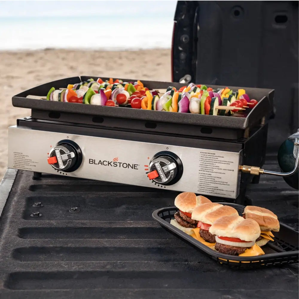 Blackstone 22in Griddle with skewers and burgers on a vehicle's open trunk.