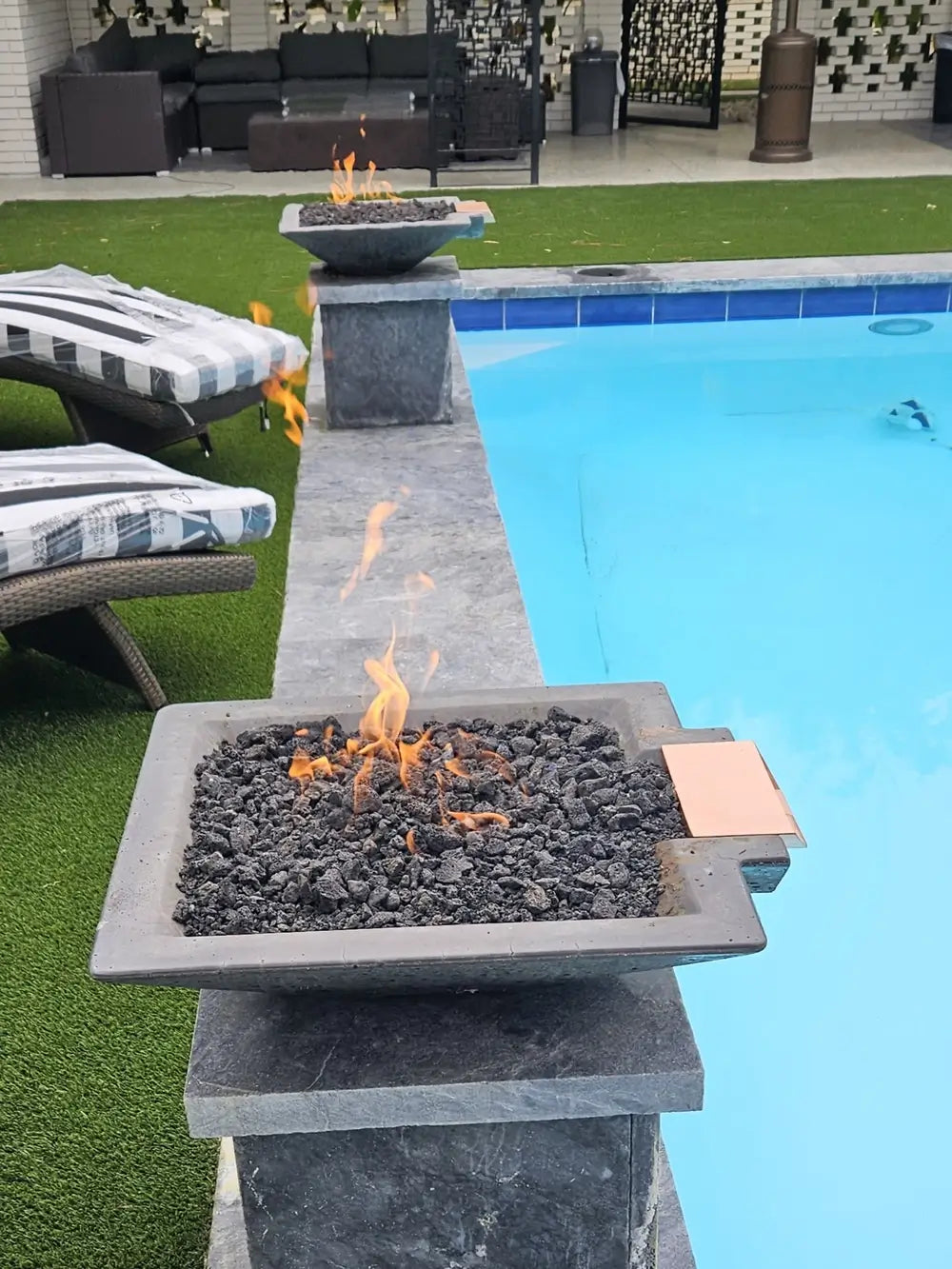 Pair of Travertine TessaRai Square Fire/Water Bowl Kits with lava rock flames on matching poolside pedestals
