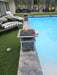 Travertine TessaRai Square Fire/Water Bowl Kit on dark stone pedestal beside pool with turf deck and striped loungers